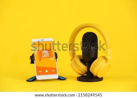 Mobile phone with word PODCAST on screen, microphone and headphones on yellow background