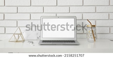 Workplace with modern laptop near white brick wall