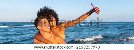Multiracial young loving couple taking a selfie together on smartphone on beach – positive fun self portrait travelling multiethnic couple in love – happy travelling couple making a selfie - horizonta