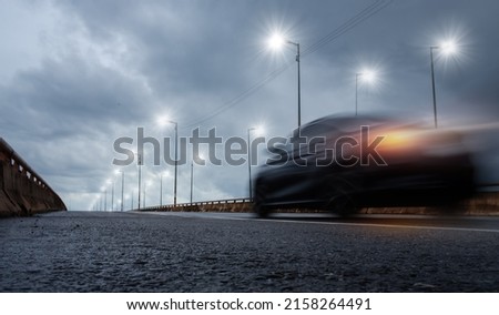 Blurry of car driving fast on bridge during hard rain with storm clouds as background,selective focus and long shutter speed exposure.Concept of rainy season,transportation and travel.