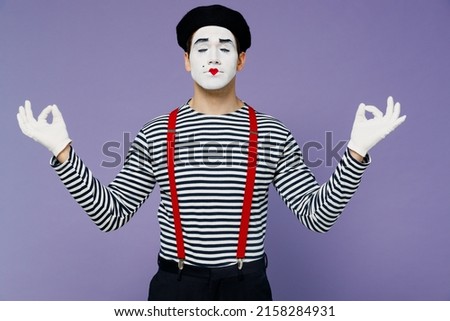Spiritual fun young mime man with white face mask wears striped shirt beret gloves hold spreading hands in yoga om aum gesture meditate isolated on plain pastel light violet background studio portrait