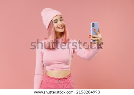 Young woman 20s with bright dyed rose hair in rosy top shirt hat doing selfie shot on mobile cell phone isolated on plain light pastel pink background studio portrait. People lifestyle fashion concept