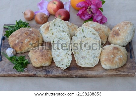 Ciabatta, Italian bread buns. Bread texture of home baked ciabatta cut in half. Ciabatta sandwich breads with leeks on wooden board; parsley garlic, onions, appes and peony flower in background.