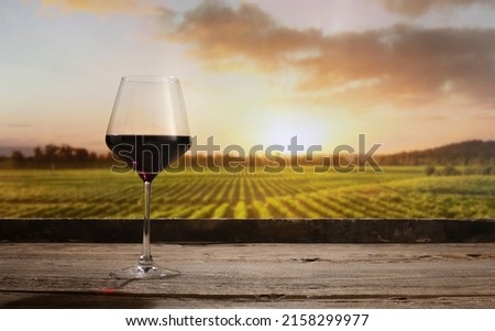 Summer evening time. Still life with red wine glass on wooden table over background of panoramic view of lush vineyards at sunset. Tasting, festivals, sophisticated lifestyle and winemaking concept Royalty-Free Stock Photo #2158299977