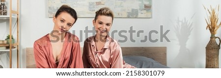 happy pangender couple in sleepwear looking at camera in bedroom, banner
