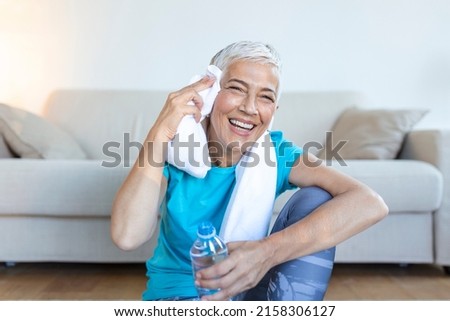 Senior woman holding plastic bottle of water,wiping sweat with a towel, exhausted after the daily training. Royalty-Free Stock Photo #2158306127