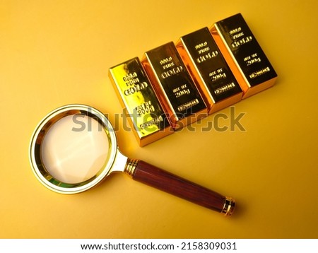 A top view of vintage magnifying glass and gold bars on a yellow background