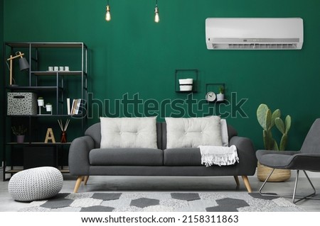 Modern air conditioner on green wall in living room with stylish furniture