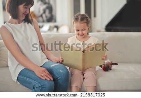 mother and daughter on the sofa look at a picture book