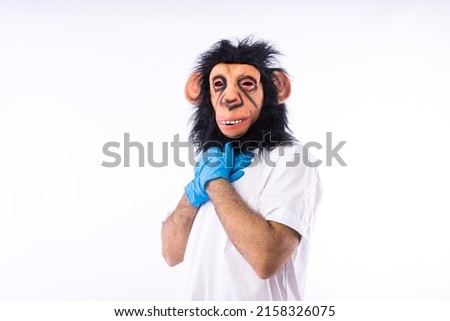 Person dressed in a monkey mask, in a medical nurse's suit, with his hands on his chest, grieving, on a white background. MONKEYPOX, Pandemic, virus, epidemic, Nigeria and smallpox. Royalty-Free Stock Photo #2158326075