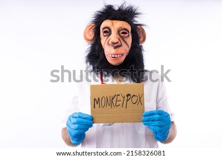 Person dressed in a monkey with a mask, with a medical nurse's suit, with a sign that reads: 'MONKEYPOX', and a syringe, on a white background. Pandemic, virus, epidemic, Nigeria and smallpox concept. Royalty-Free Stock Photo #2158326081