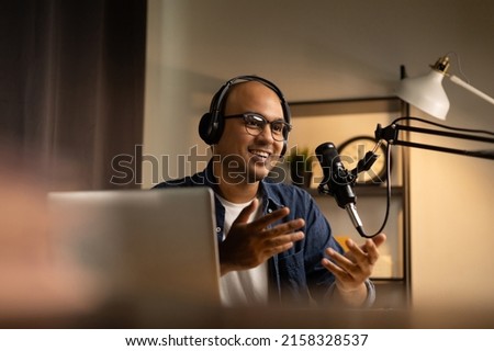 Young asian man host streaming podcast with condenser microphone work on laptop at small broadcast home studio. Content creator blogger recording voice over radio interview guest conversation Royalty-Free Stock Photo #2158328537