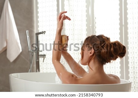 Beautiful woman with sponge taking bath indoors