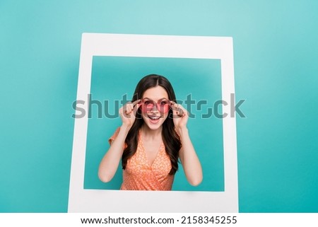 Photo of excited funky woman wear orange outfit eyewear looking inside paper frame isolated turquoise color background
