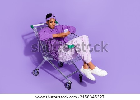 Full length photo of trans bisexual hipster male sit shopping cart surfing in telephone isolated on violet color background Royalty-Free Stock Photo #2158345327