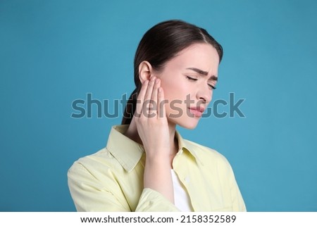 Young woman suffering from ear pain on light blue background Royalty-Free Stock Photo #2158352589