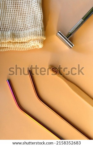 Reusable metal straws, wooden toothbrush, reusable safety razor and mesh bag on neutral background. Flat lay.