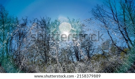 Close-up view of streams of fountain with reflection and lens flare. Water jet. City fountain. Water pressure. How to survive the heat. Splashes shining in the sun. Selective shallow focus.