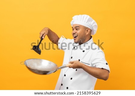 Young handsome asian man chef in uniform holding turner and iron Frying pan utensils cooking in the kitchen various gesture on yellow background. Indian man Occupation chef restaurant and hotel.
