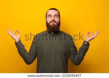 Young bearded man holding hands for zen gesture over yellow background.