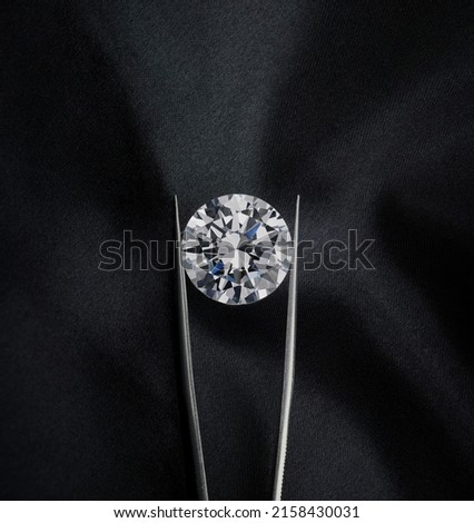 Round Diamond Held in Tweezers Upright on Luxury Black Background.    Royalty-Free Stock Photo #2158430031