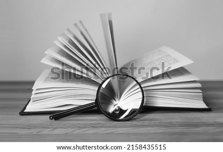 Open book with magnifying glass. Turning pages. Information search and analysis, research conducting concept. Black and white. High quality photo