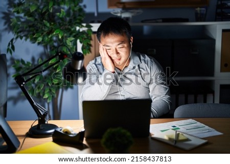 Young chinese man working using computer laptop at night thinking looking tired and bored with depression problems with crossed arms. 