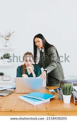 two young business women professionals in formal wear clothes work in modern office using laptop, tablet, brainstorm and search for solutions together, confident independent Asian girl solves problems