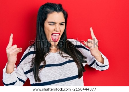 Young hispanic girl wearing casual clothes shouting with crazy expression doing rock symbol with hands up. music star. heavy concept. 