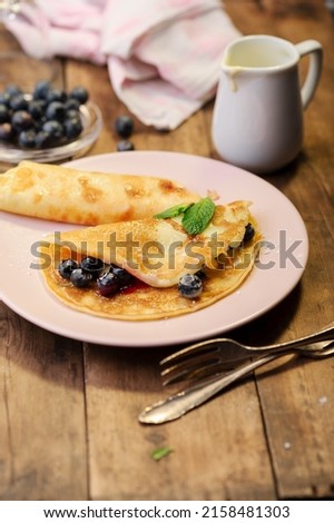 A vertical shot of fresh crepes served with blueberries and jam on a plate on a wooden table background