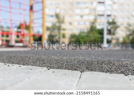 The boundary between the mulch rubber playground and the sidewalk tiles. Transition to the area for sports and playground. View of the blurred image of the yard Royalty-Free Stock Photo #2158491165
