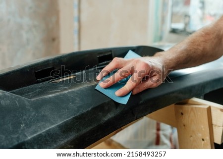 Close up of male hand polishing sanding with sandpaper a car bumper. First step before painting car's plastic bumper cover. Selective focus. Royalty-Free Stock Photo #2158493257