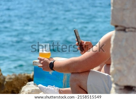 A closeup of a man sitting in a beach bar and taking a picture of the beer