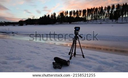 A camera on tripod making time-lapse photography stuck in the snow during sunset in Vantaa