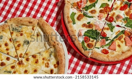 Partial top view of two different pizzas on plates on tablecloth over table in cafe or restaurant. Unhealthy eating and fast food. Fresh baked delicious and appetizing junk food for lunch and leisure
