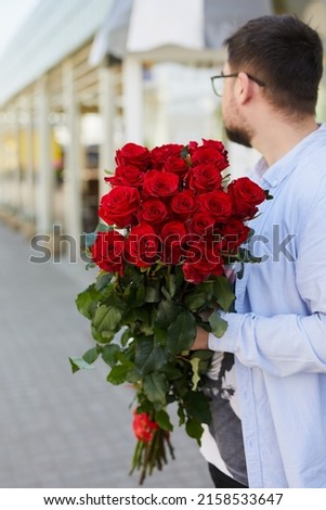 a young guy in a plaid shirt and glasses with a large bouquet of roses