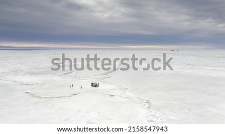 Aerial view to the cracked ice seascape with a unidentified group of people skating and exploring on the ice bank, transported in safely by using hydr