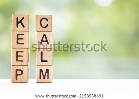 KEEP CALM - word is written on wooden cubes on a green summer background. Close-up of wooden elements.