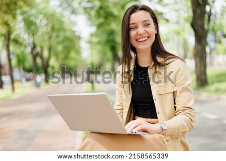 A woman uses a laptop while walking in the park.