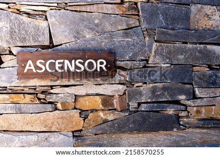 A closeup of a stone wall with a wooden sign saying "ascensor" which means elevator in Spanish