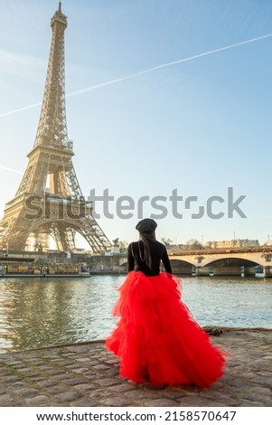A vertical shot of a Black young female in front of the Eiffel Tower