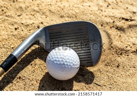 A closeup of a ball with a golf stick on the sand under sunlight