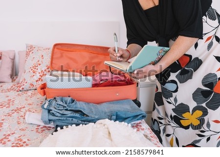 cropped shot of a mature blonde woman, jotting down in her diary the items of luggage she is taking for her trip. business woman preparing her trip.