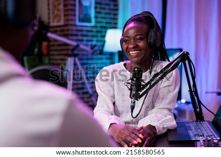 Female influencer interviewing guest on podcast stream, using recording equipment. Happy woman streaming live broadcast episode with man in studio to record conversation for channel.