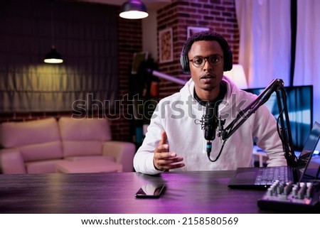 POV of young influencer recording podcast episode on camera, talking into microphone for sound production. Male blogger filming livestream vlog to create social media web content. Royalty-Free Stock Photo #2158580569