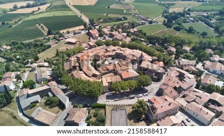 An aerial shot of a medieval round village with red tile roofs surrounded by green fields and trees