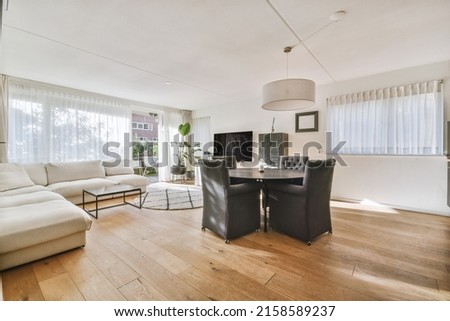Comfortable armchairs and couch placed near lamps and shelf with TV and dining zone with kitchen against window in modern living room Royalty-Free Stock Photo #2158589237