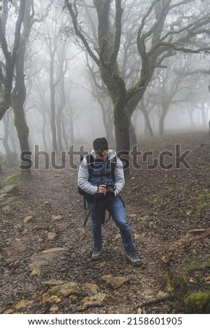 A vertical shot of the young Caucasian male with the camera in his hands in the forest