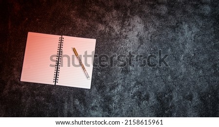 A top view of a blank notepad with a pen on a gray background