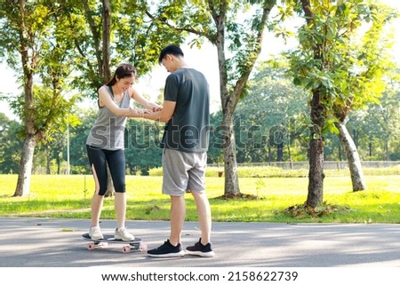 Asian couple exercising together in the morning Practice basic skateboarding on the streets of the park. Playing sports for health makes you strong and happy.